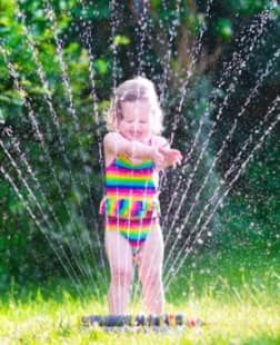 Little girl playing with garden sprinkler