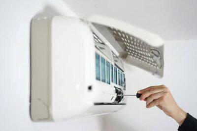 Person's hand screwing in a screw while installing a ductless air conditioner system on a home's white wall.