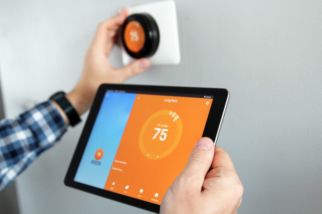 A person adjusting temperature using a tablet with smart home app in modern living room. Smart thermostat on wall in background.